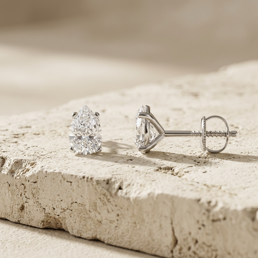Profile of the pear diamond studs showing the martini setting and screw back on cream concrete