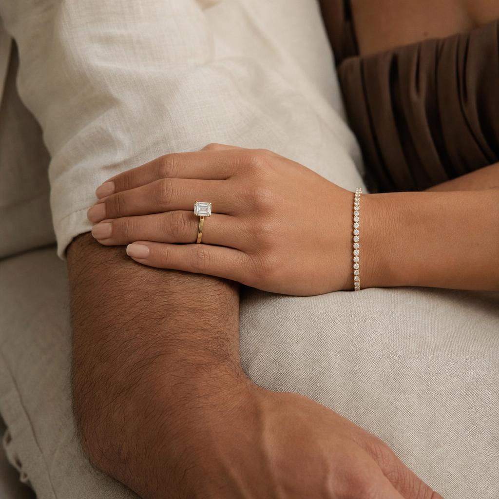 Couple's hands with a diamond tennis bracelet and emerald-cut solitaire ring