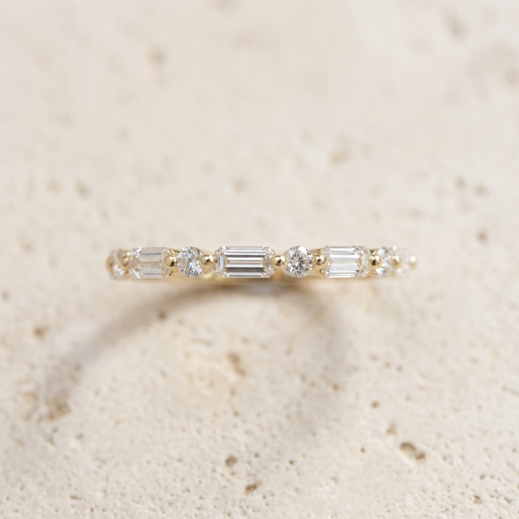 Front view of The Sequence band, alternating baguette and round diamonds on cream concrete